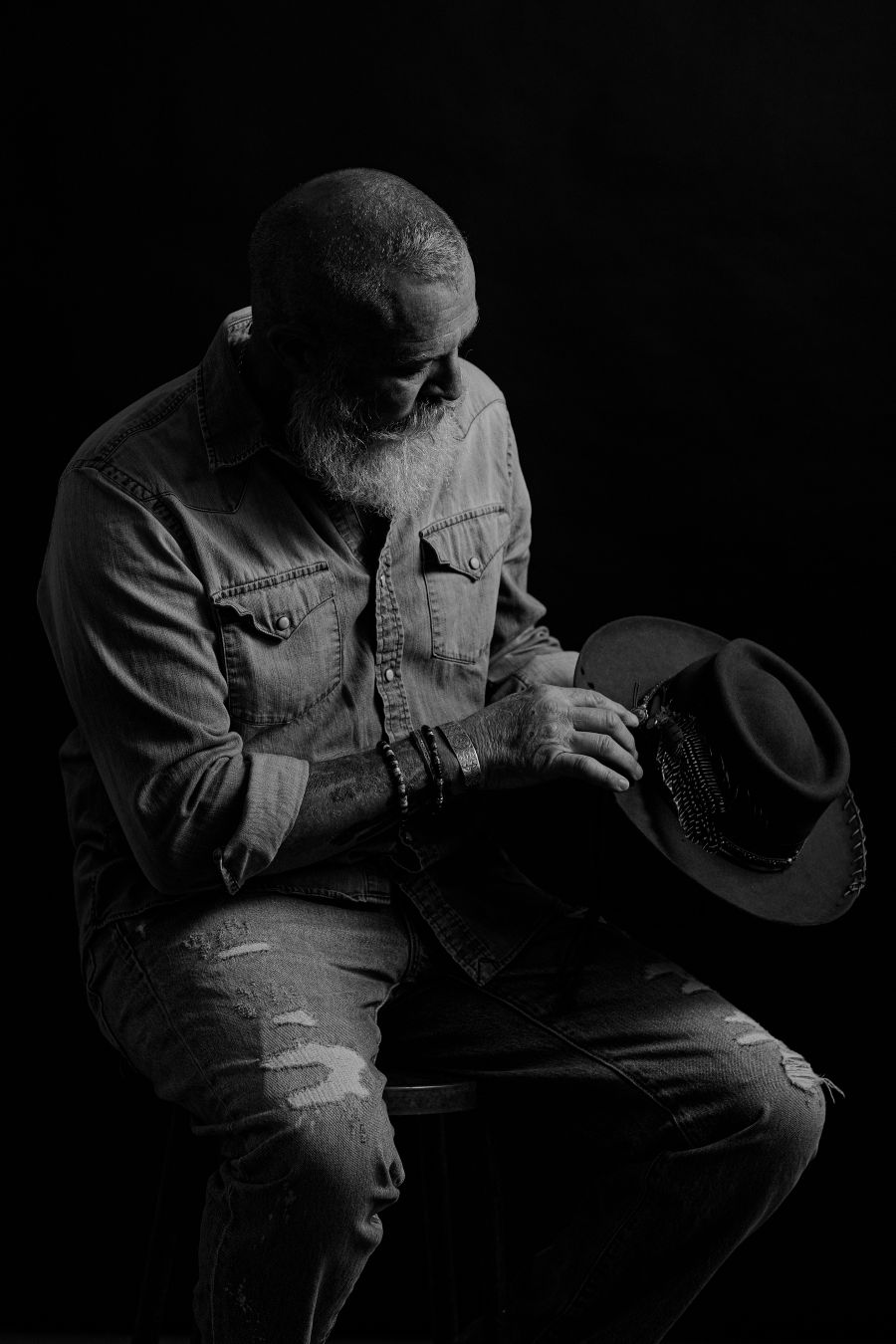 Monochrome study of seated figure examining dark hat in contemplative pose.