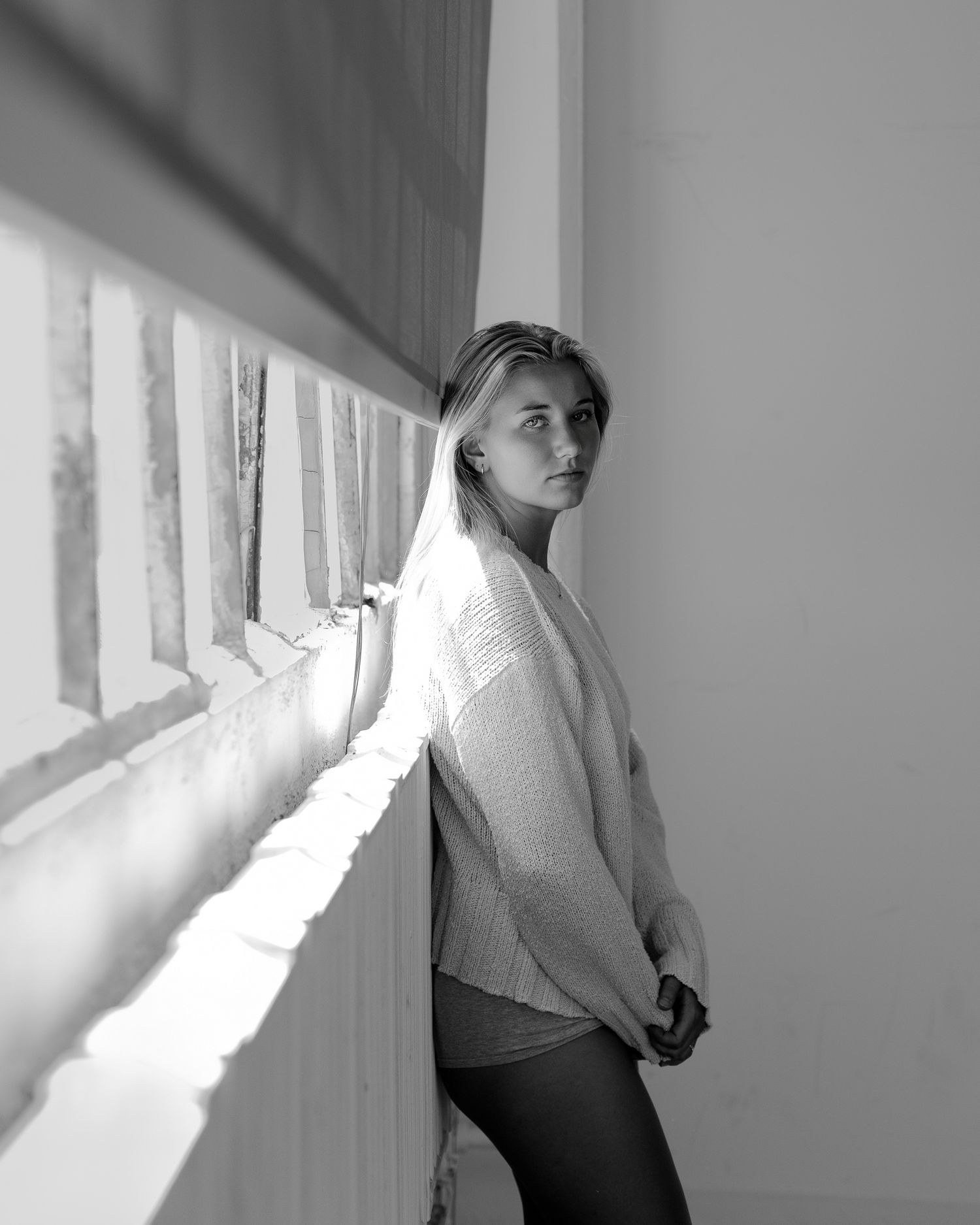 Minimalist photoshoot with dramatic window lighting and white clothing against pale walls.
