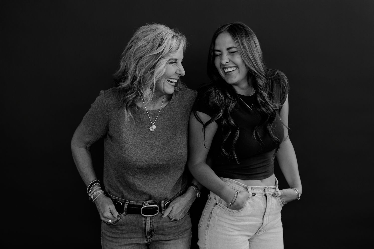 Two women in contrasting outfits expressing joy during a black and white photoshoot.