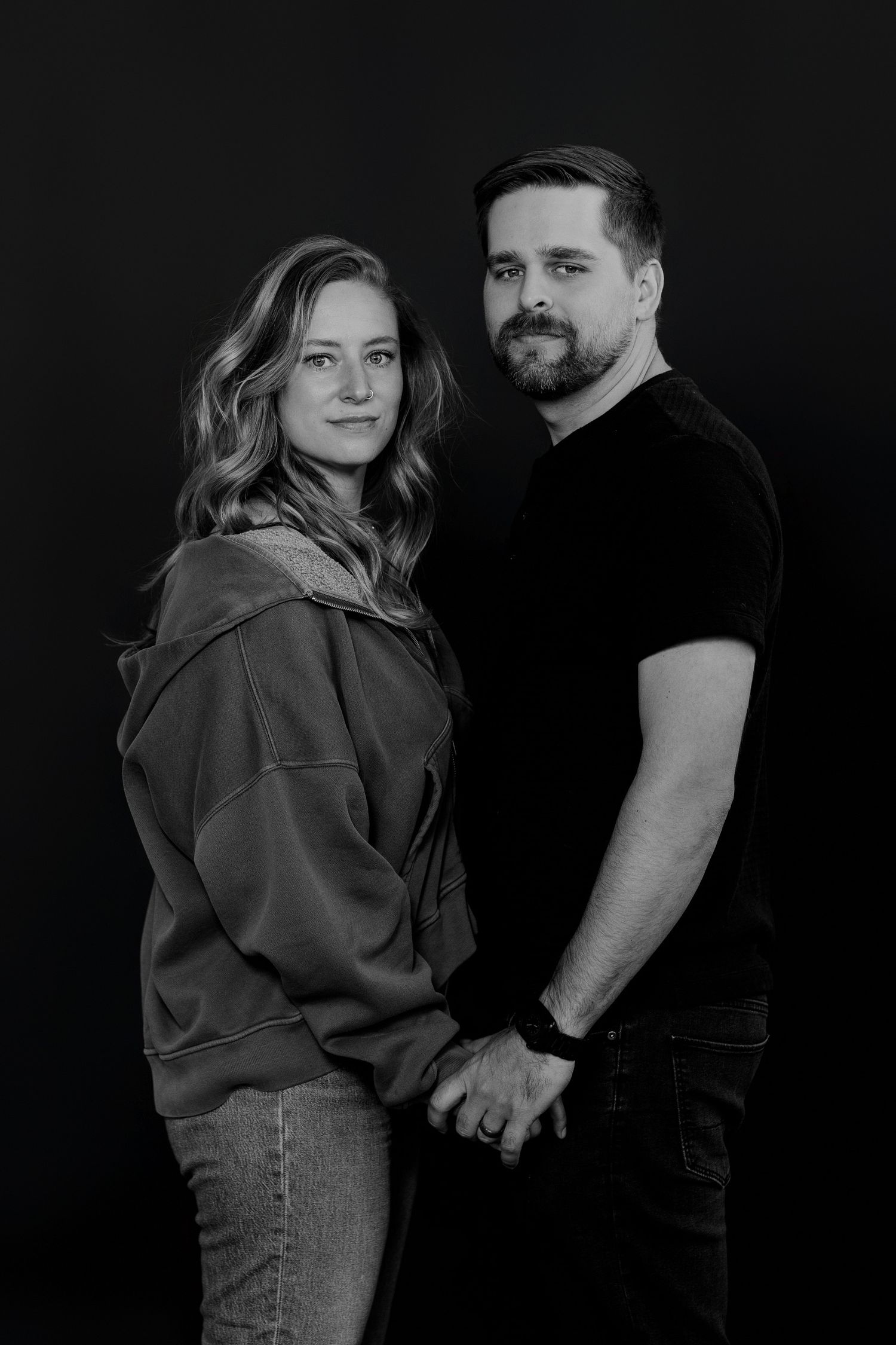 Stylish couple in casual attire posing together for black and white studio portrait.