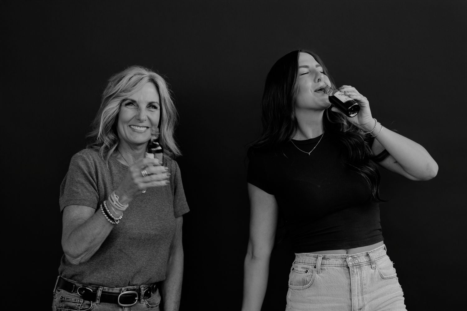 Two women in casual outfits sharing a candid moment against a dark backdrop.