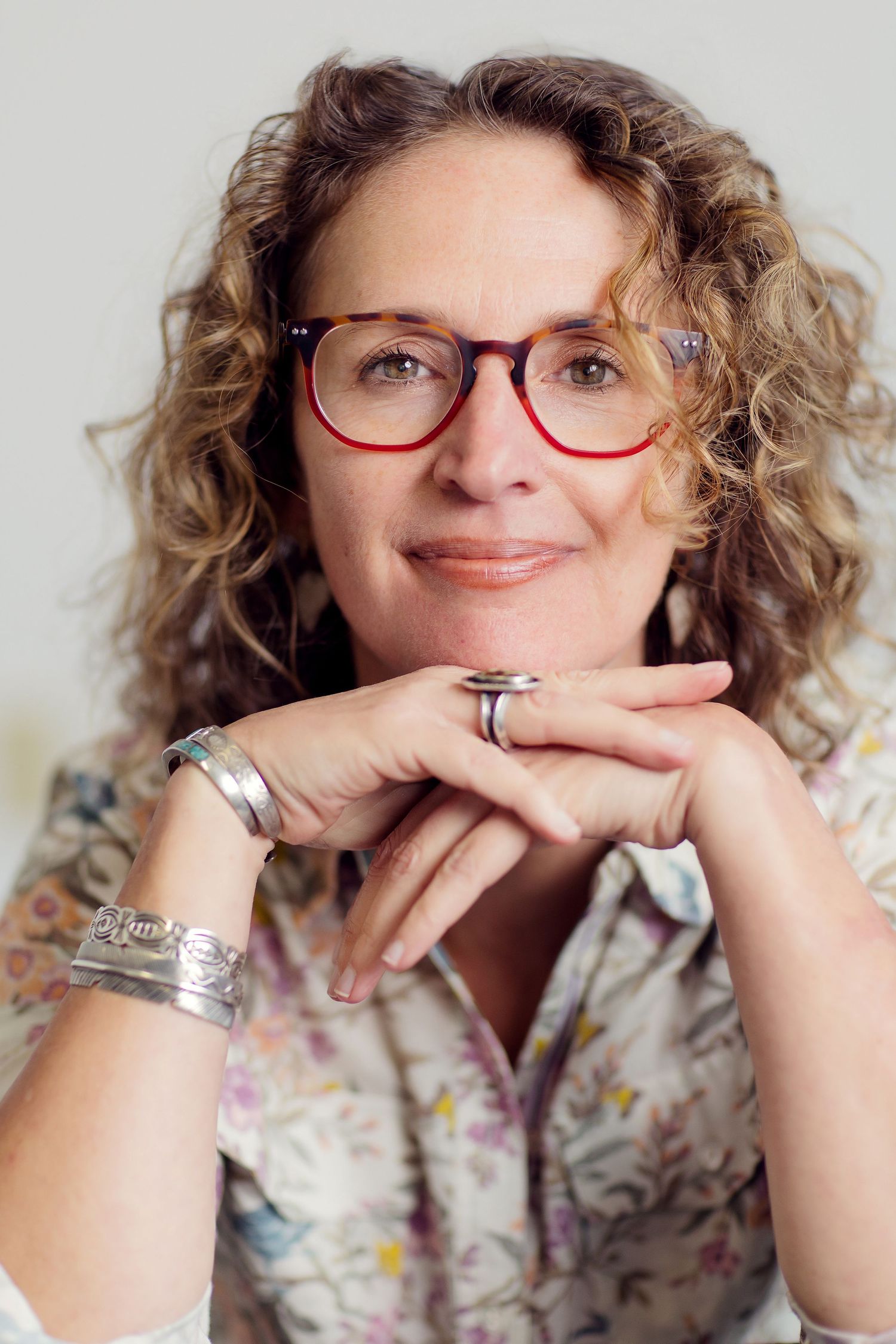 A series of expressive portraits showing someone with curly hair wearing red glasses and a floral print top, resting on their hands.