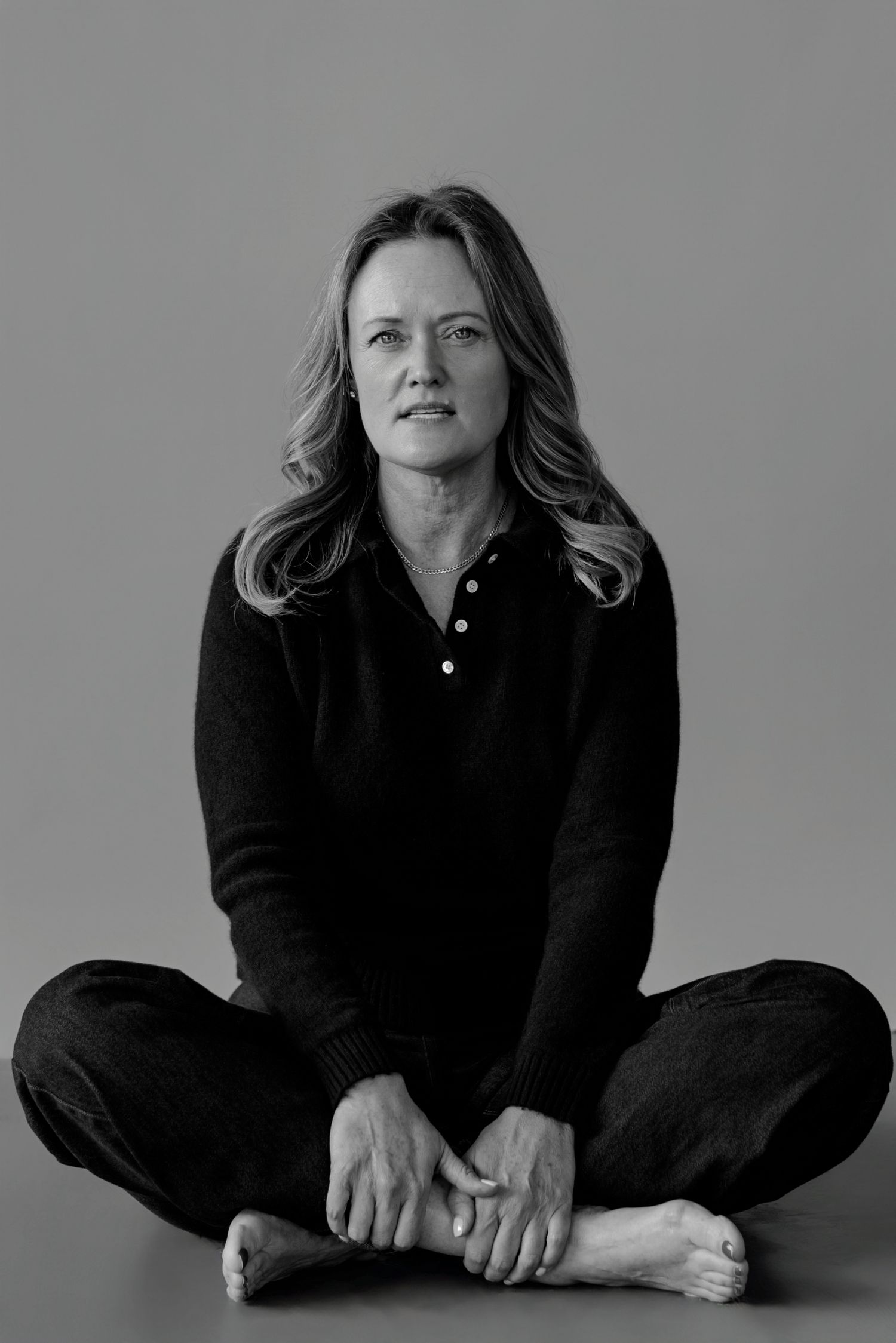 Figure in black outfit seated cross-legged on light backdrop in monochrome series.