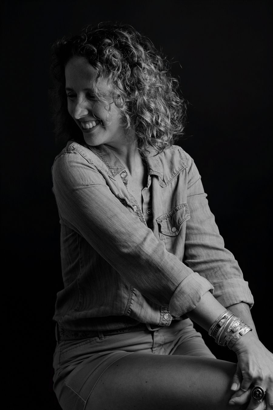 Dramatic portrait of a person in light colored clothing sitting against a dark background.