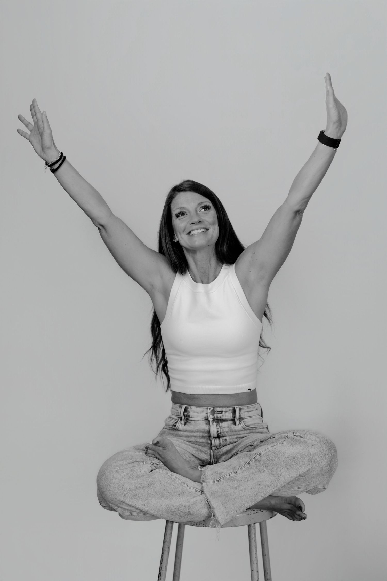 Person in white tank top and jeans showing energetic poses while sitting.