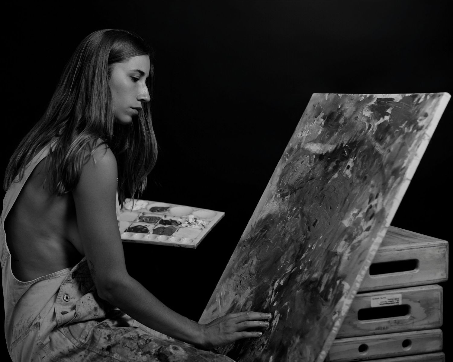 Figure examining paint-splattered artwork panels in monochrome lighting.