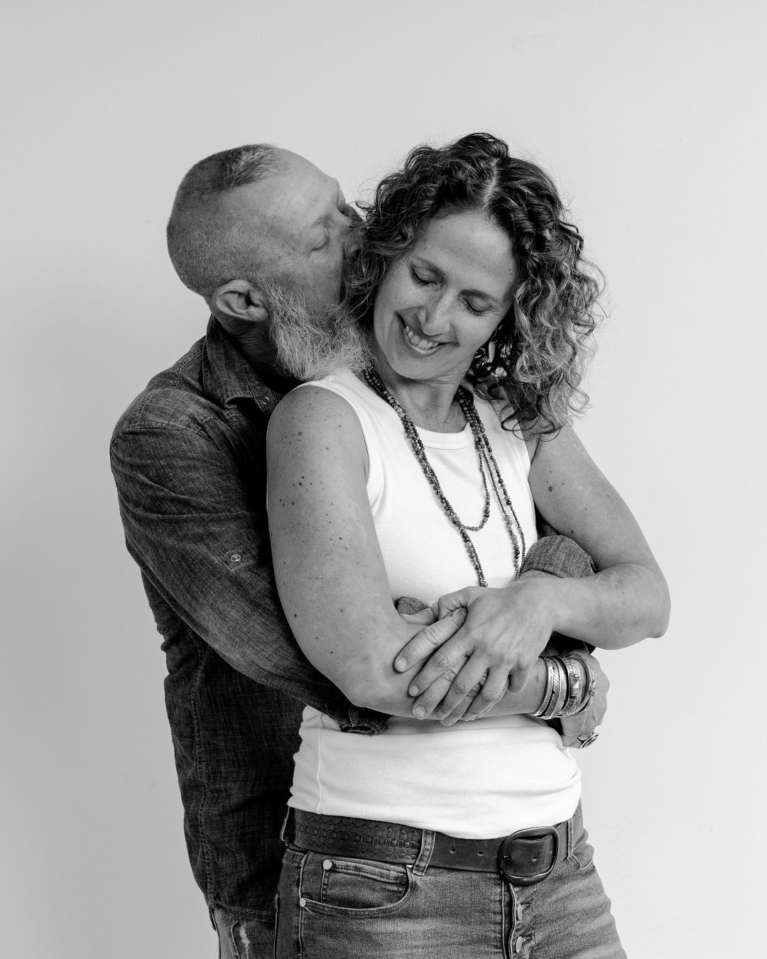 Intimate black and white photoshoot showing couple embracing in casual attire against white background.