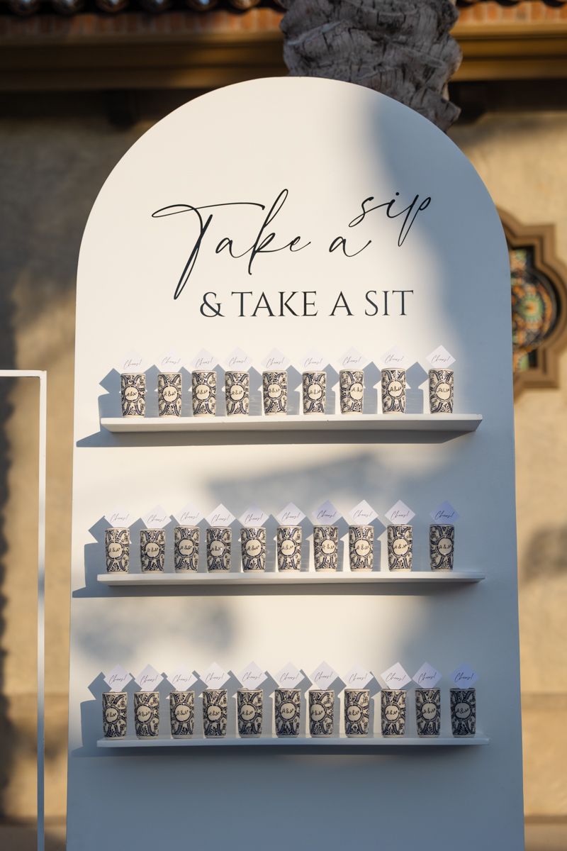 White arched wedding seating chart display with small favor boxes on shelves.