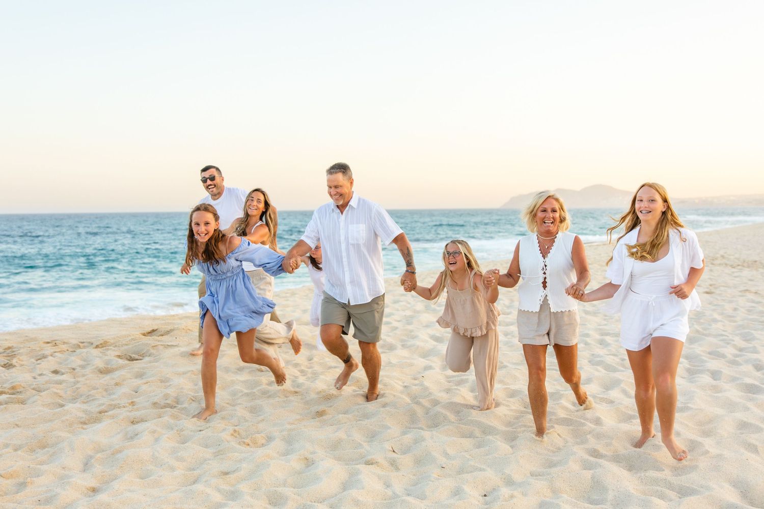 Happy family of seven running and holding hands on a sunny sandy beach with ocean waves in the background.