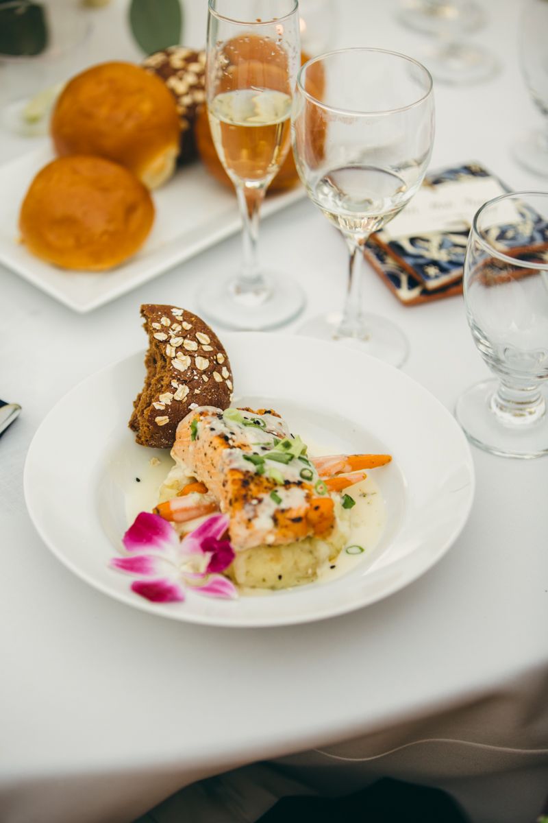 Plated salmon dish with vegetables and orchid garnish served with champagne at a wedding reception.