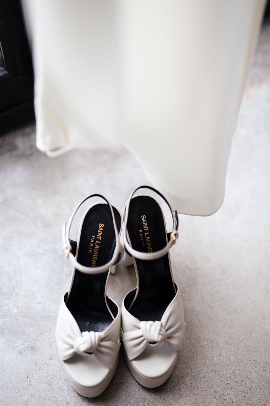 Saint Laurent white platform heels with bow detail placed beside a flowing white wedding gown.