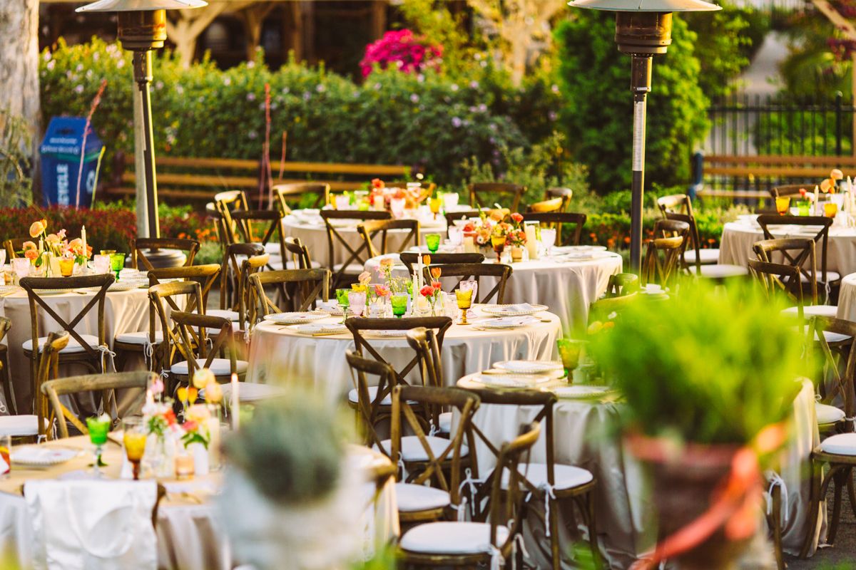 Elegant outdoor wedding reception with round tables, wooden chairs, and floral centerpieces.