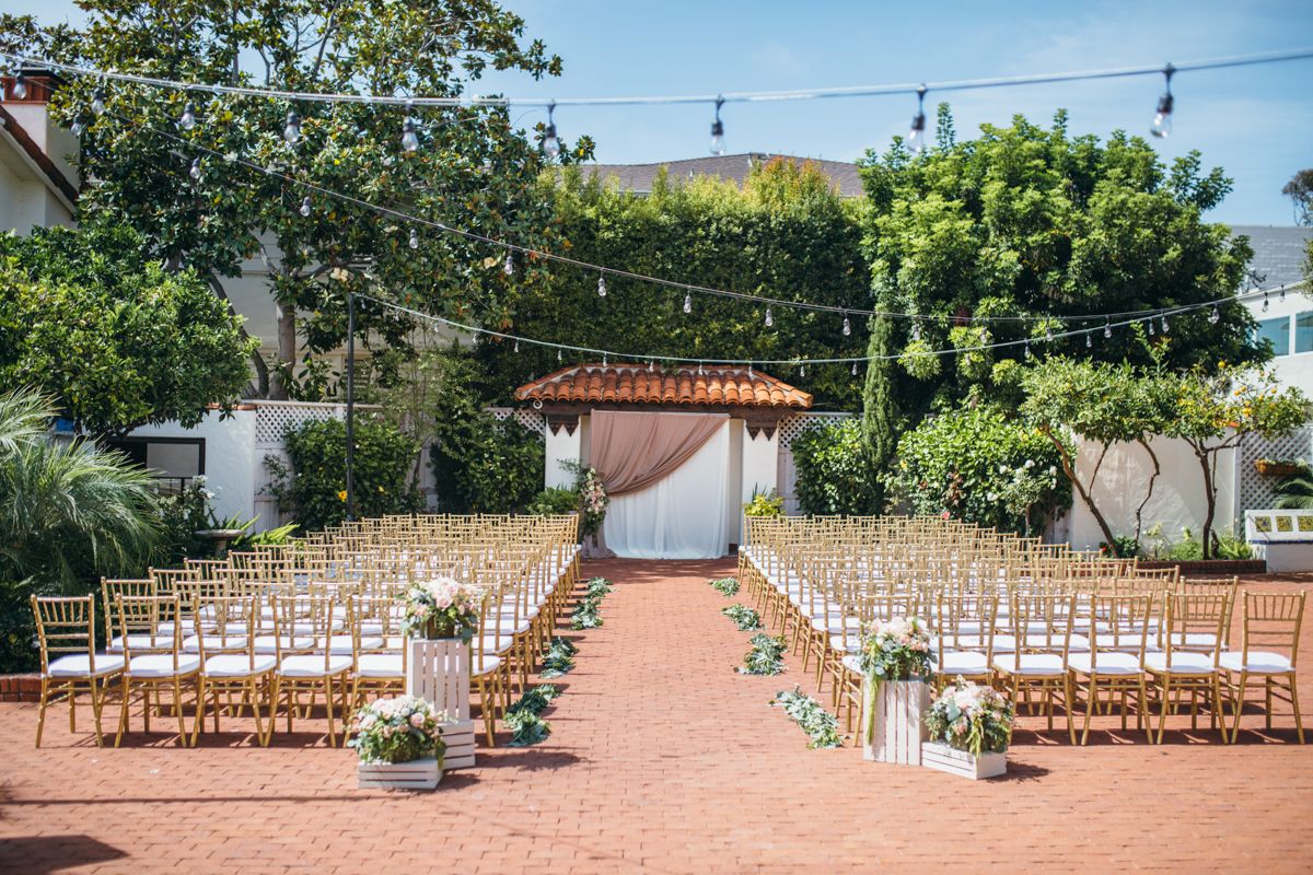 Elegant outdoor wedding ceremony setup with gold chiavari chairs and floral aisle decorations.