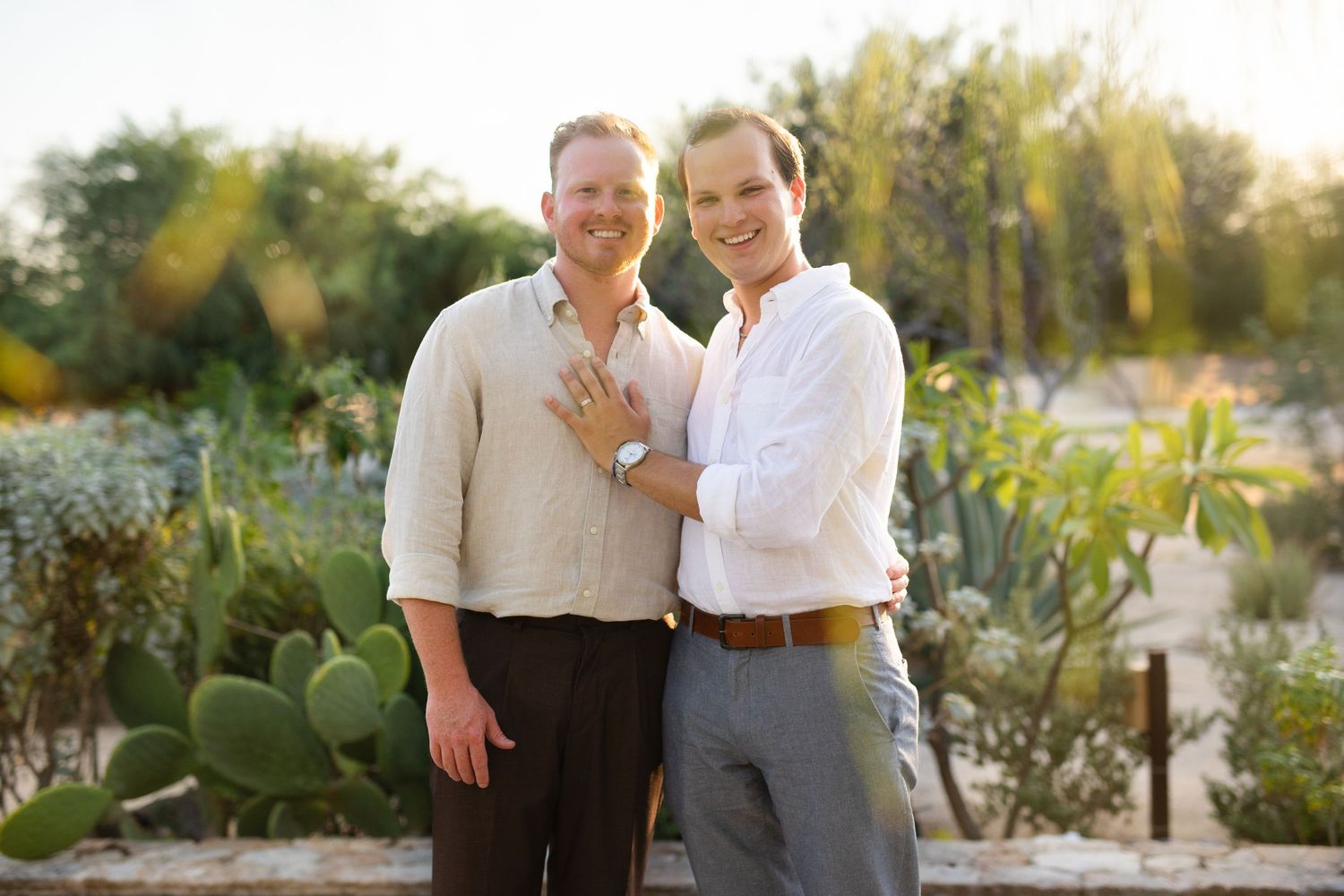 Engaged same-sex couple posing together in a desert garden, showing off engagement ring.