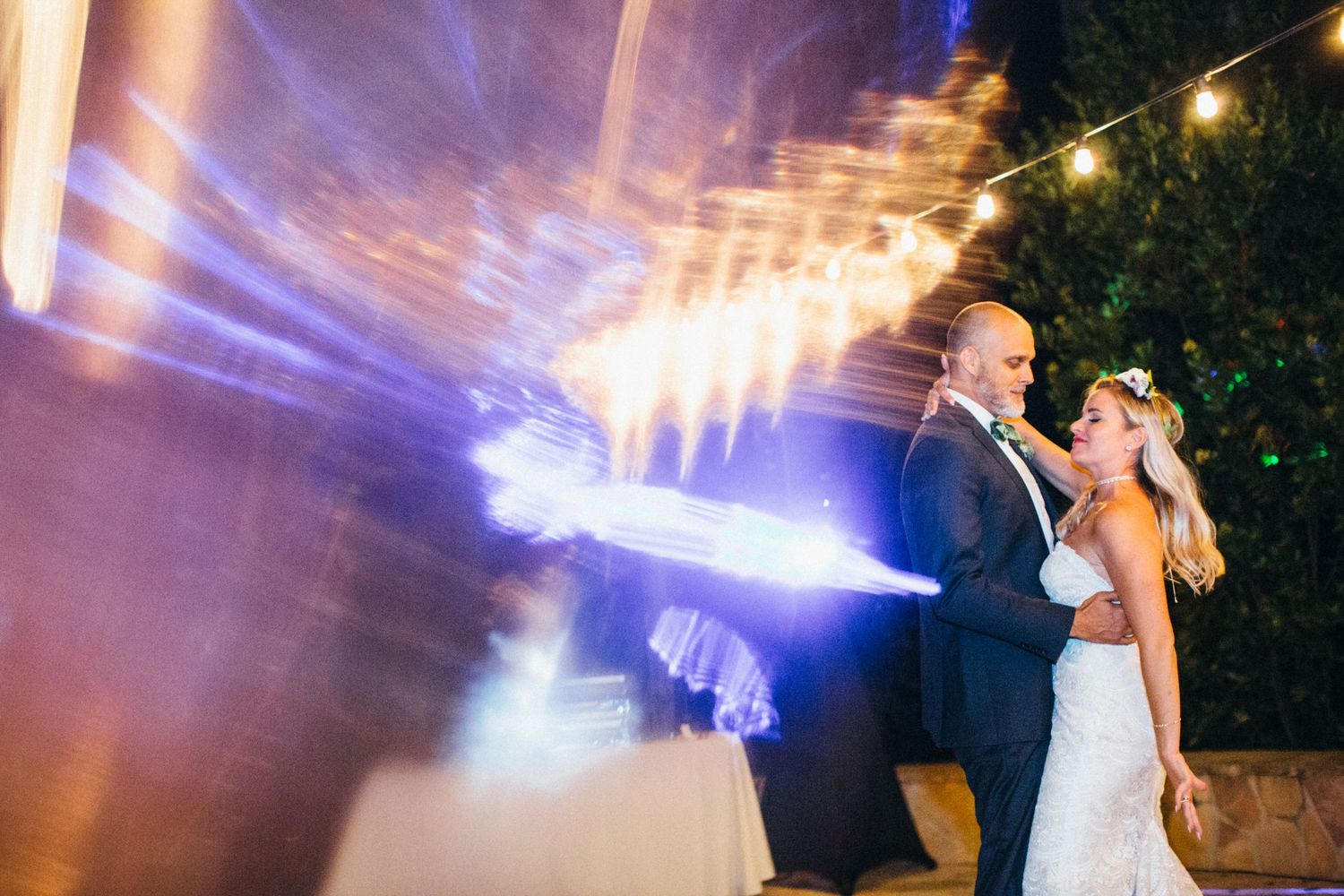 Bride and groom share romantic first dance with dramatic blue stage lighting at elegant outdoor wedding reception.