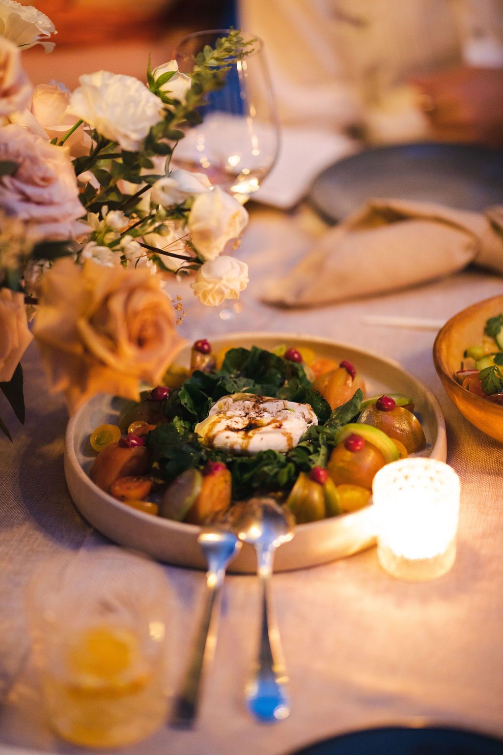 Beautiful wedding reception place setting with a gourmet salad plate, candle, and white floral centerpiece.