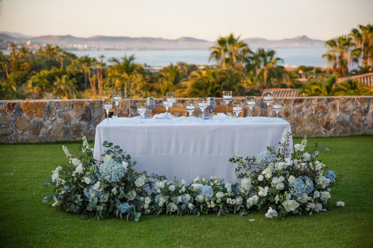 Sweetheart table with white linen and lush blue and white floral arrangements at sunset.