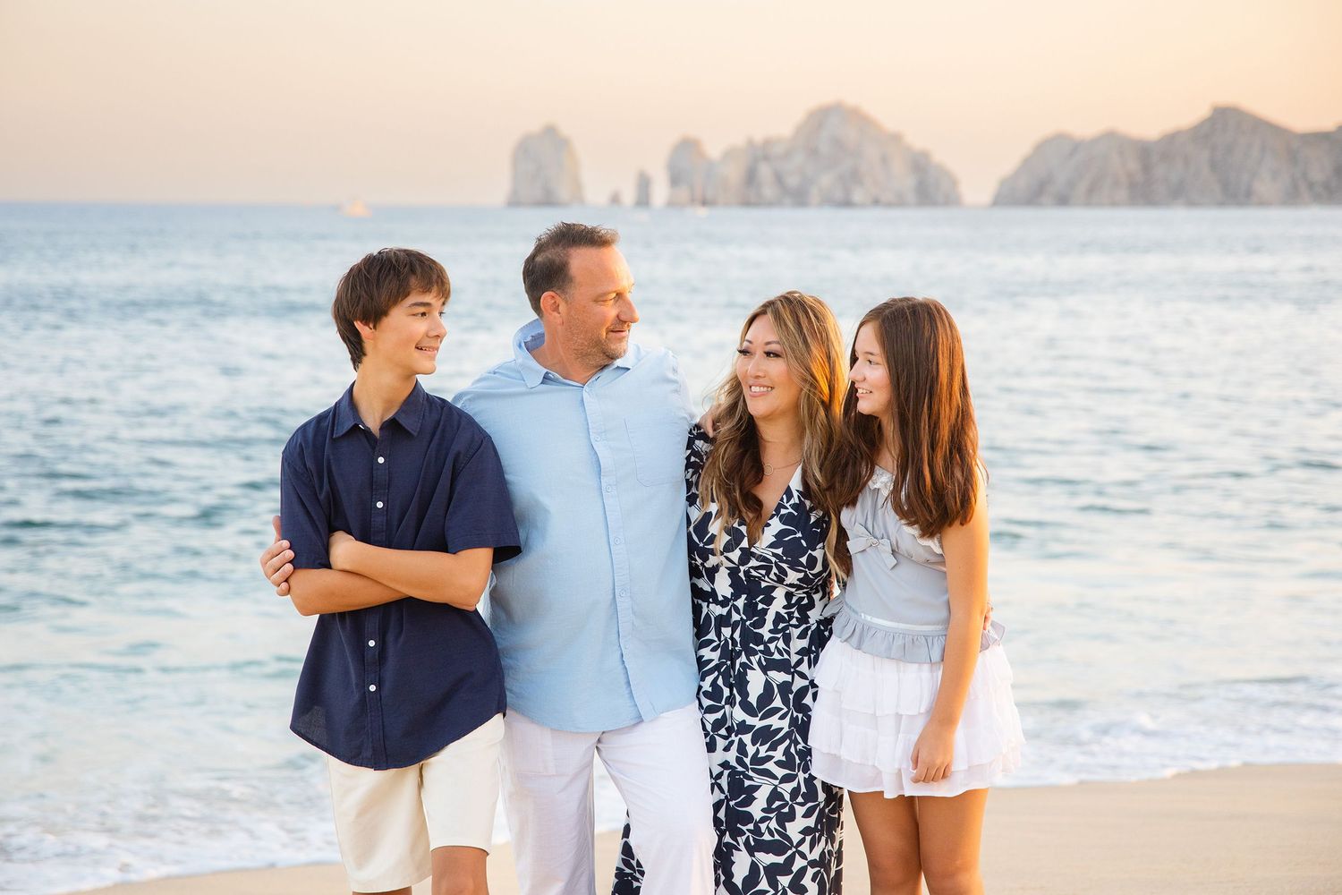 Family of four sharing a joyful moment on a scenic beach with rocky cliffs in the background.