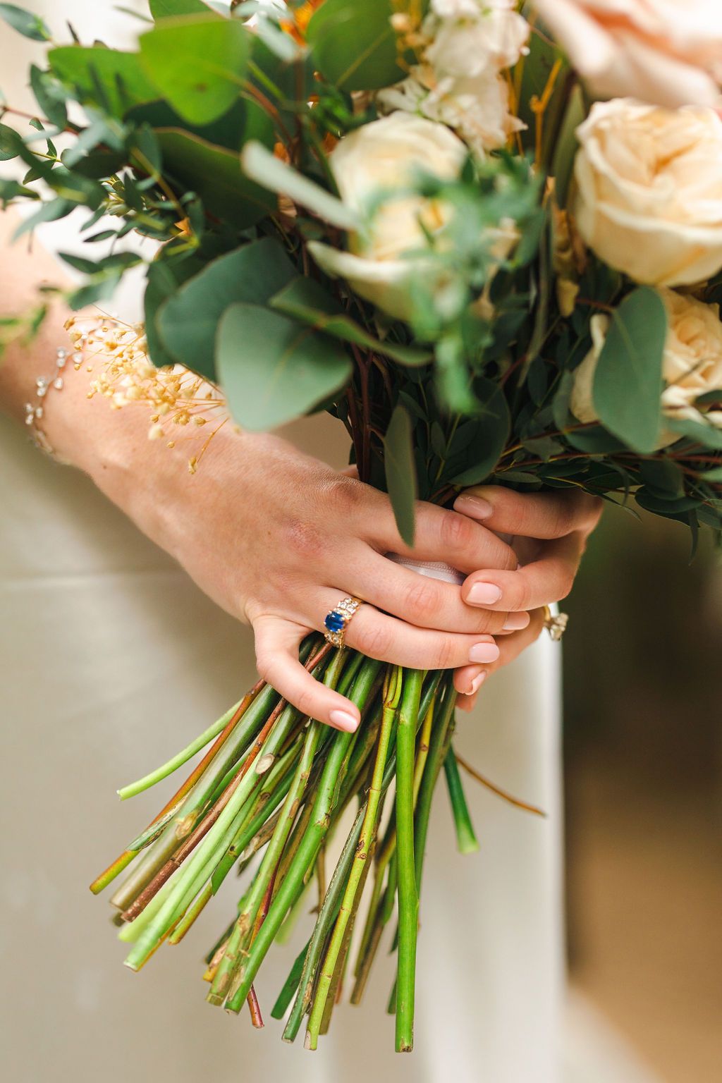 Bride holding a lush bouquet of white and peach roses with a sapphire and diamond engagement ring on her finger.