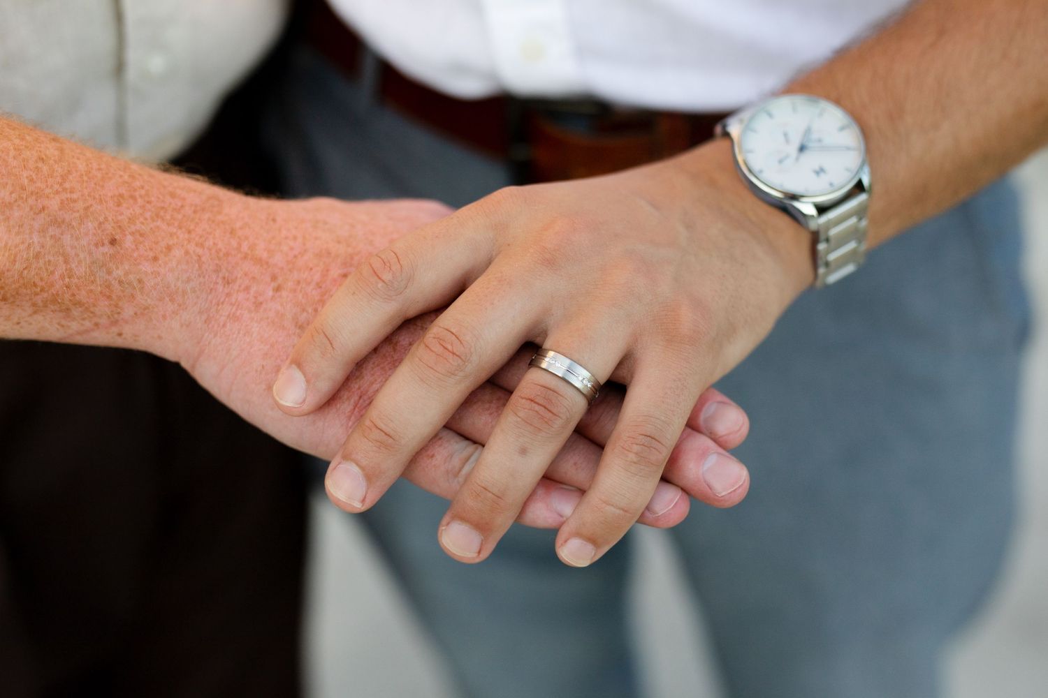Close-up of two hands together, one wearing a silver wedding band and the other a watch, symbolizing marriage.