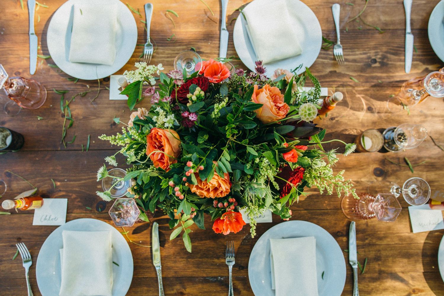 Elegant rustic wedding table setting with orange roses centerpiece, white plates, and linen napkins on wood table.