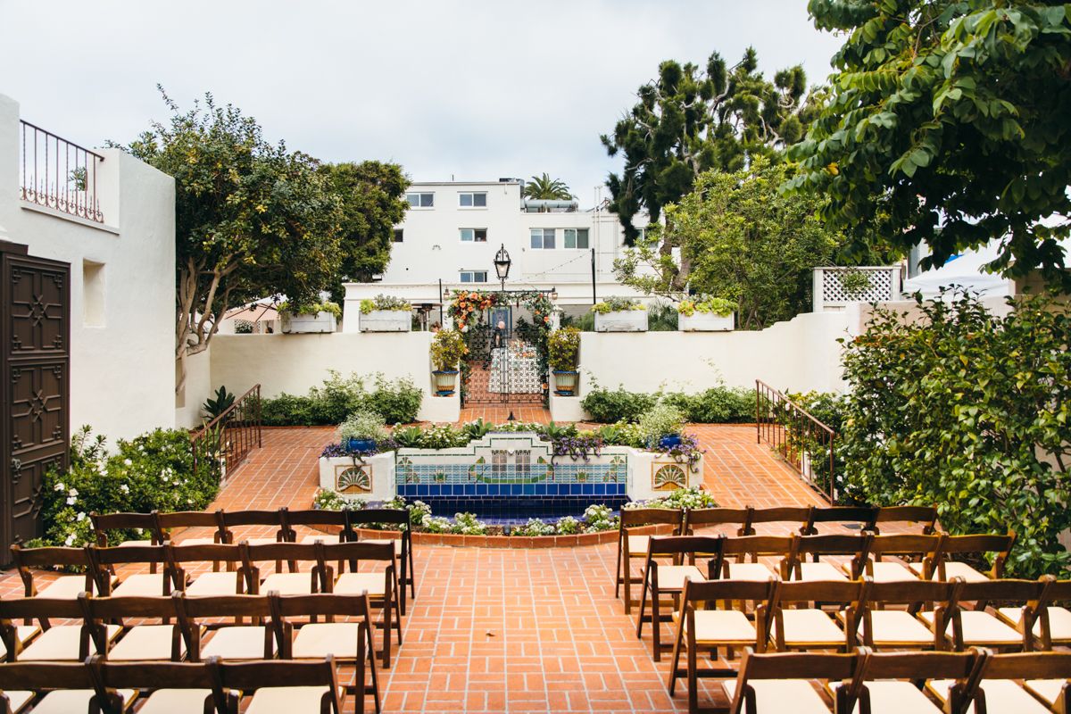 Elegant outdoor wedding ceremony setup with wooden chairs on a brick courtyard beside a decorative fountain.