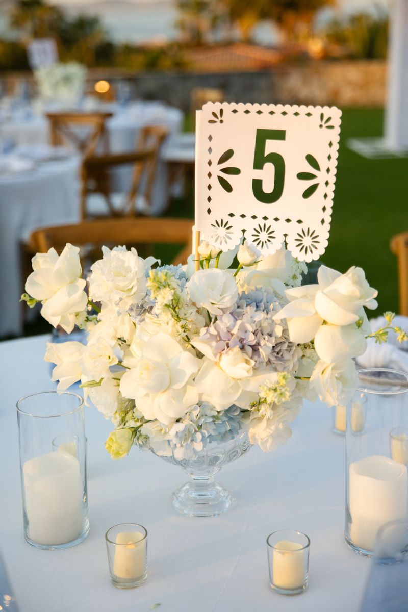 Elegant wedding centerpiece with white roses and hydrangeas beside table number five sign.