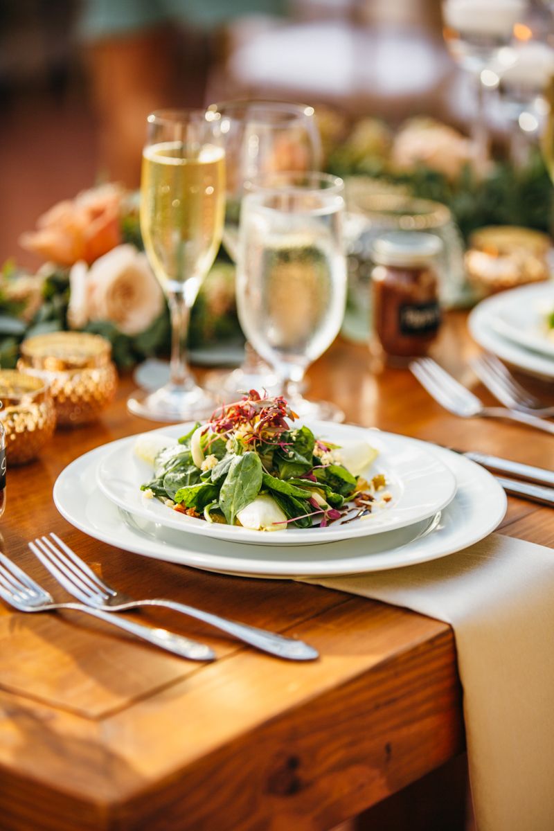 Elegant wedding place setting with fresh green salad, champagne flutes, and gold accents on a wooden table.