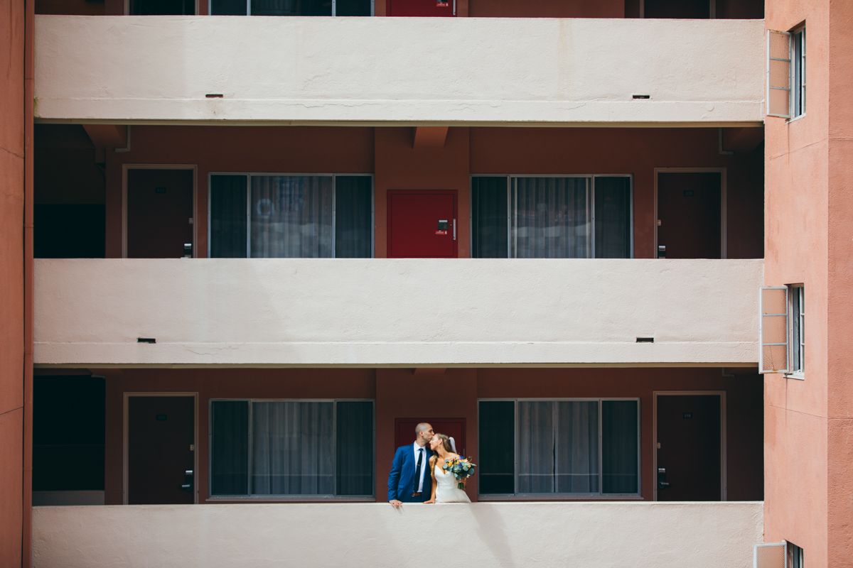 A bride and groom share a romantic moment on a balcony of a multi-story building.