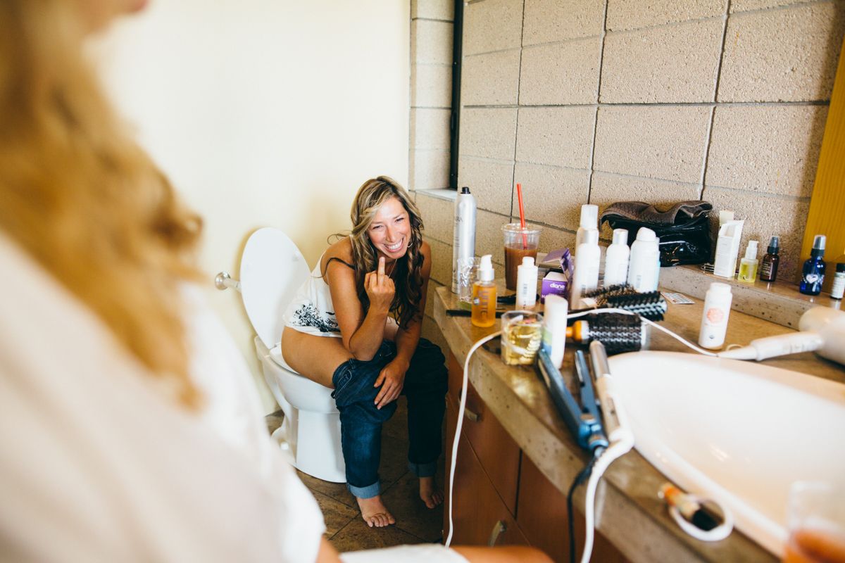 Young woman applies makeup while sitting in bathroom during wedding day preparations.