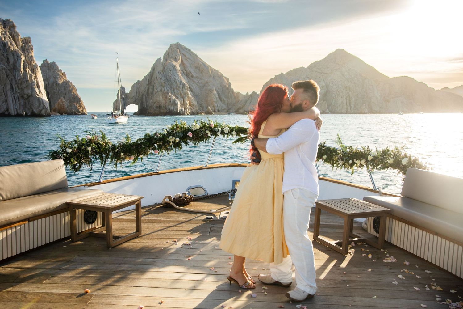 Couple kissing on yacht deck at sunset with ocean and rocky cliffs in background at Cabo San Lucas.