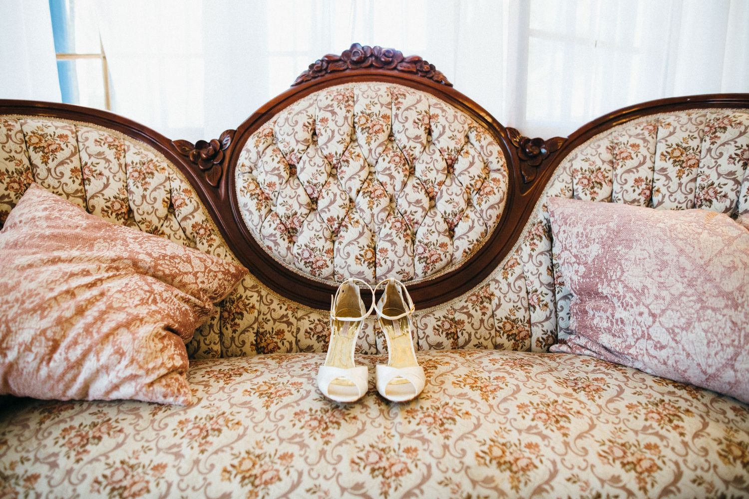 Elegant vintage floral sofa with tufted back, pink pillows, and white bridal heels displayed for a wedding Leo Carrillo ranch