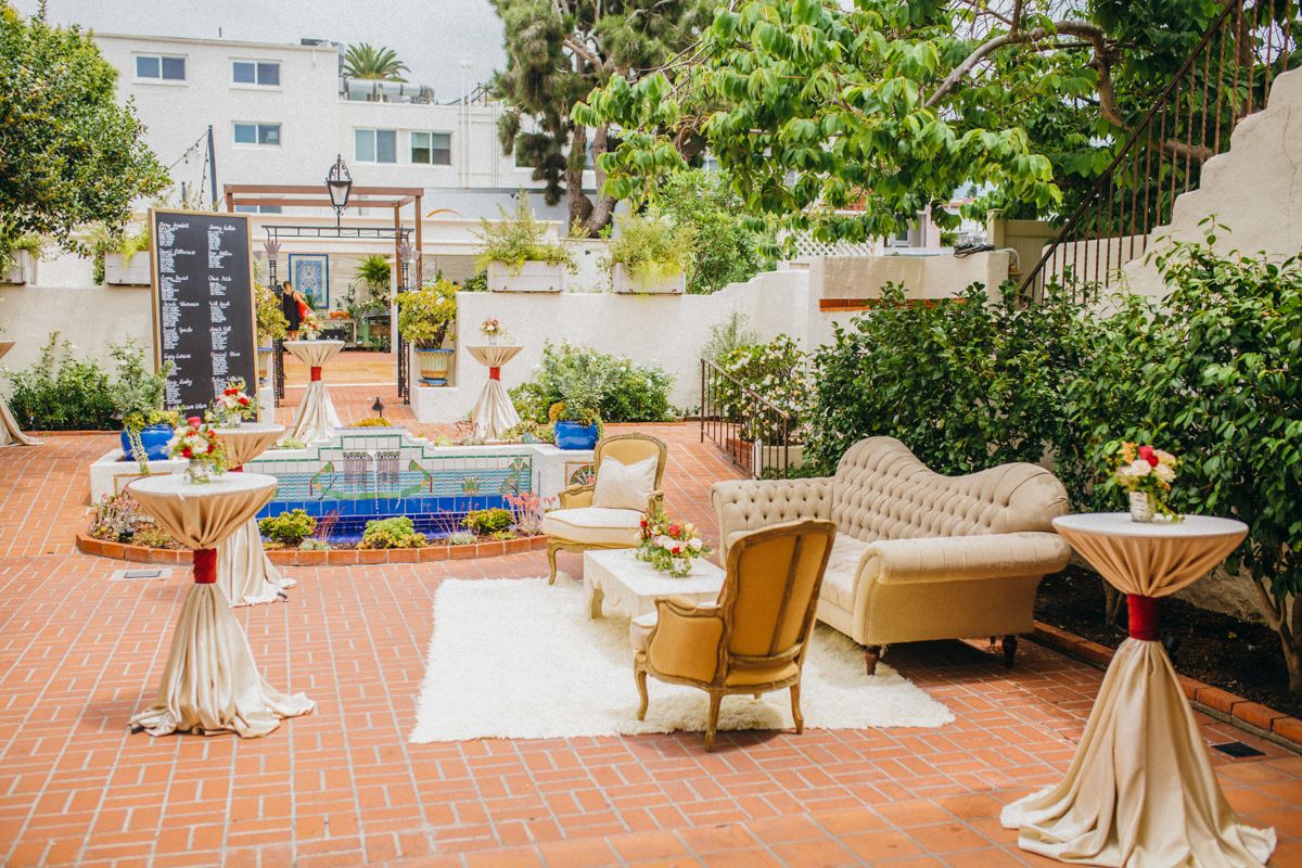 Elegant outdoor wedding cocktail hour setup with vintage furniture and cocktail tables near a tiled fountain.