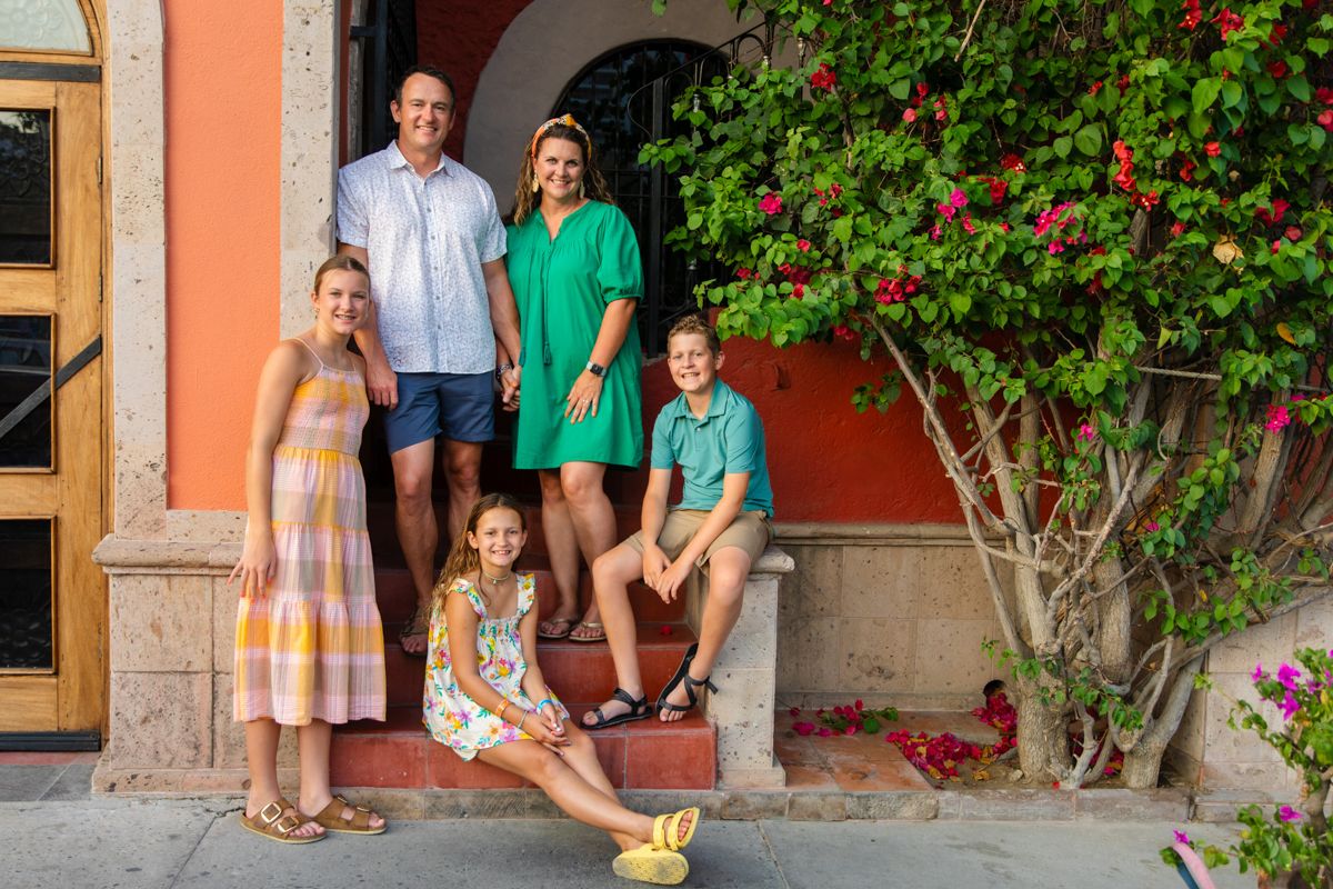Family of five posing on colorful steps beside blooming bougainvillea in Mexico.