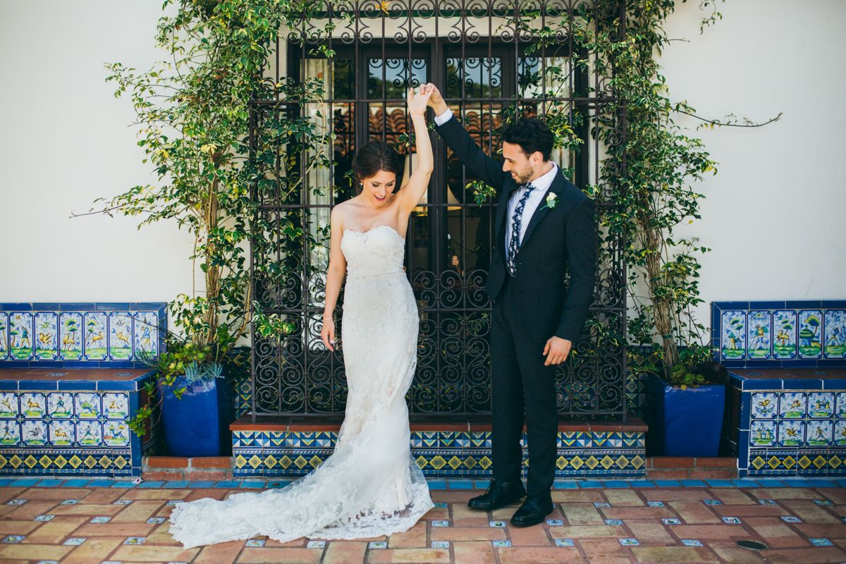 Bride and groom dance together before ornate iron gate with blue mosaic tile accents outdoors.