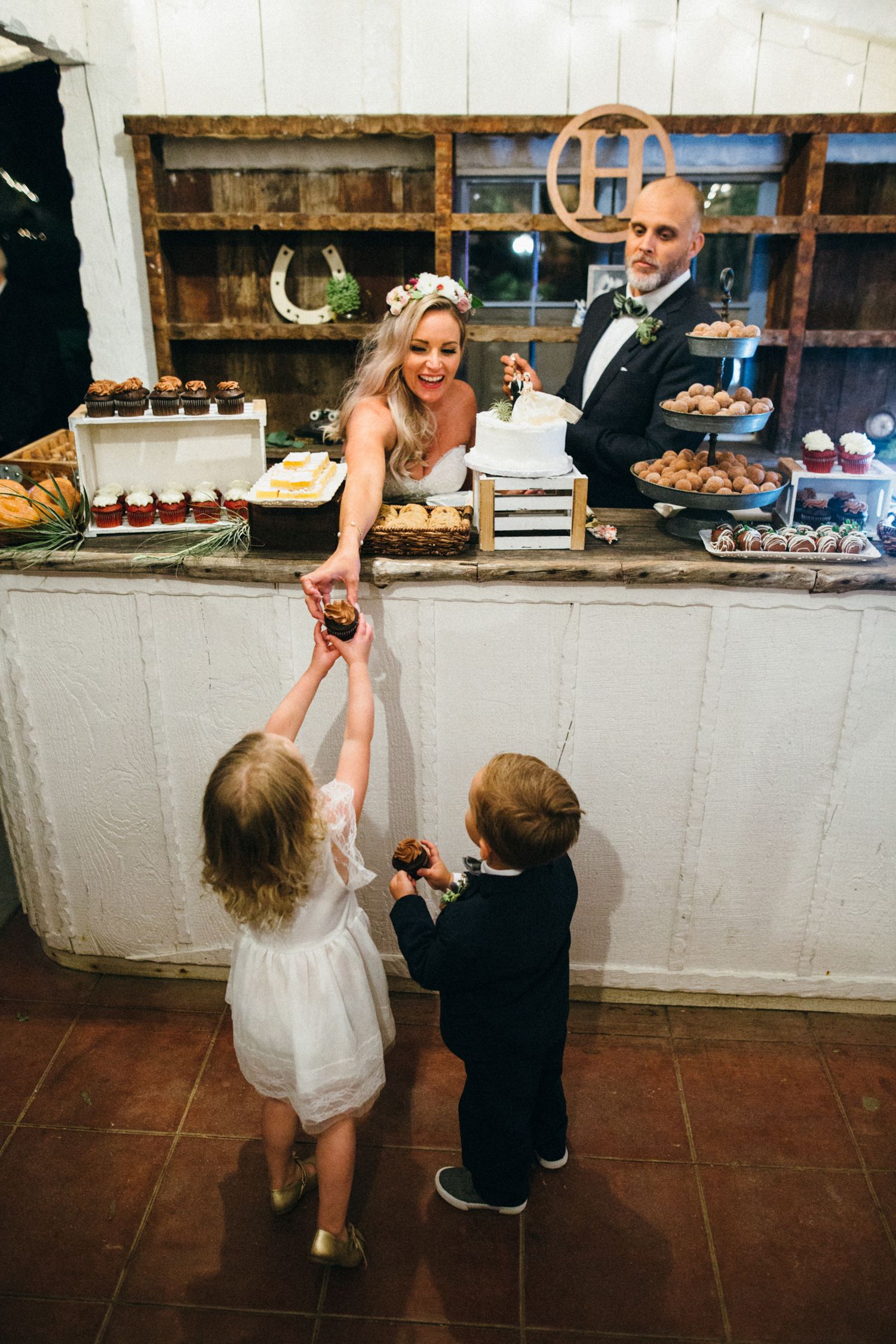 Bride and groom at wedding dessert table handing cupcakes to flower girl and ring bearer.