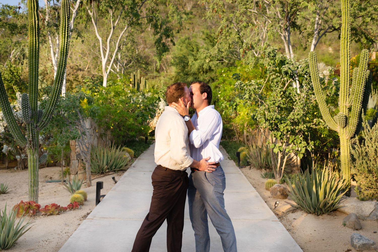 Two people sharing a romantic kiss on a garden path surrounded by cacti and lush greenery at acre resort San Jose del cabo