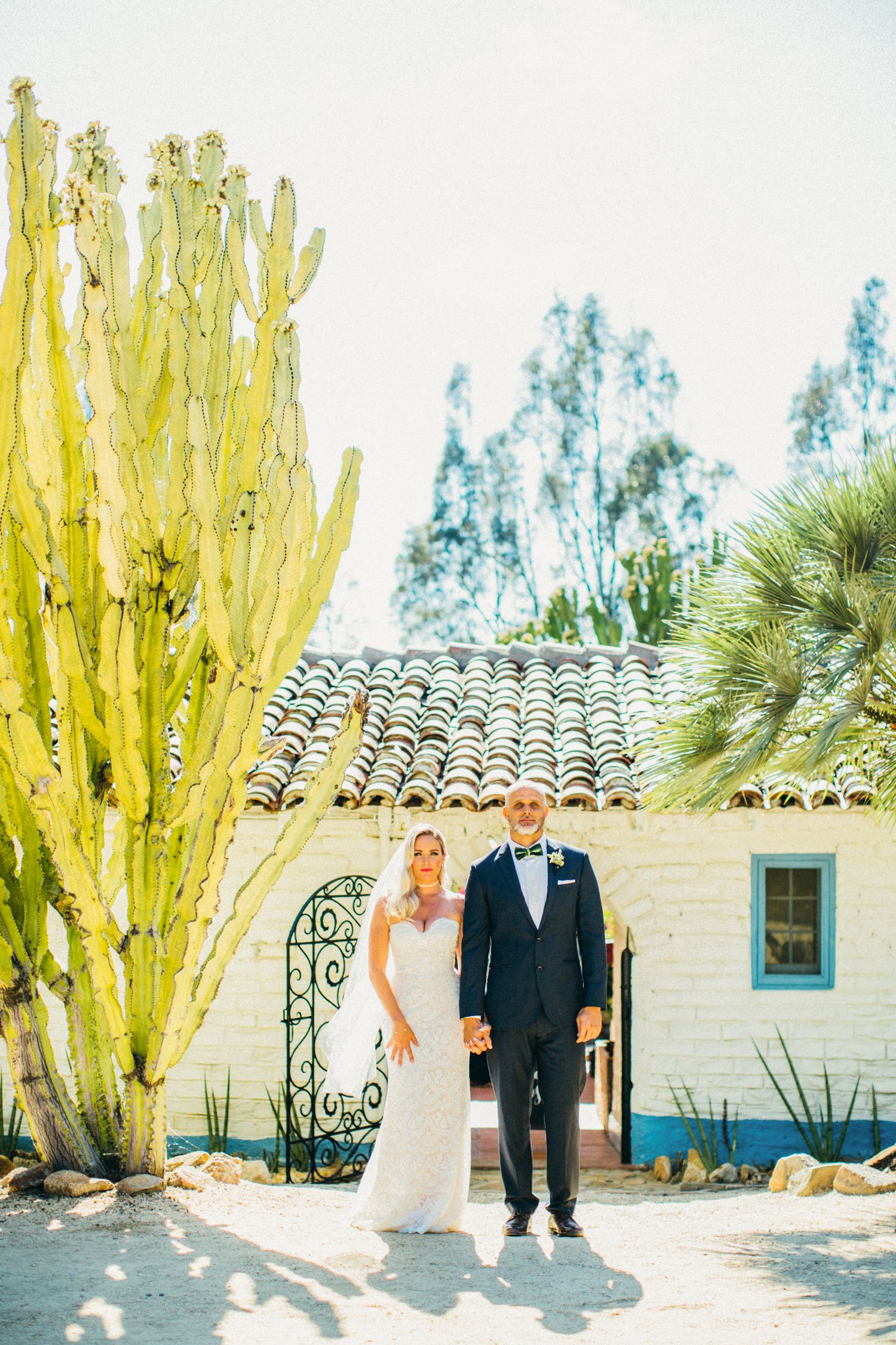 Bride and groom stand together near a tall cactus outside a Spanish-style building with terracotta roof tiles at Leo Carrillo ranch