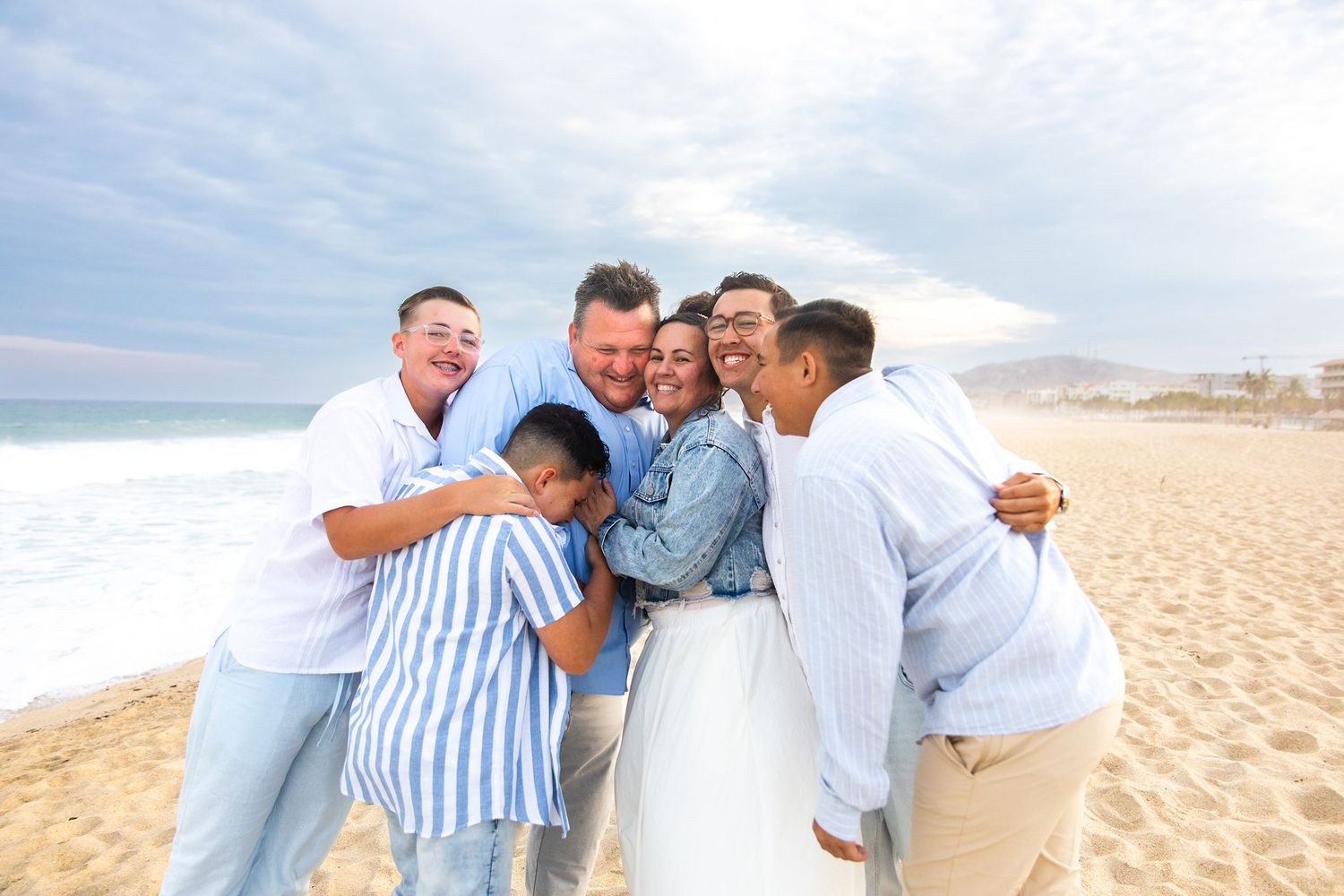 Joyful family hugging and laughing together on a sunny beach with ocean waves behind them.