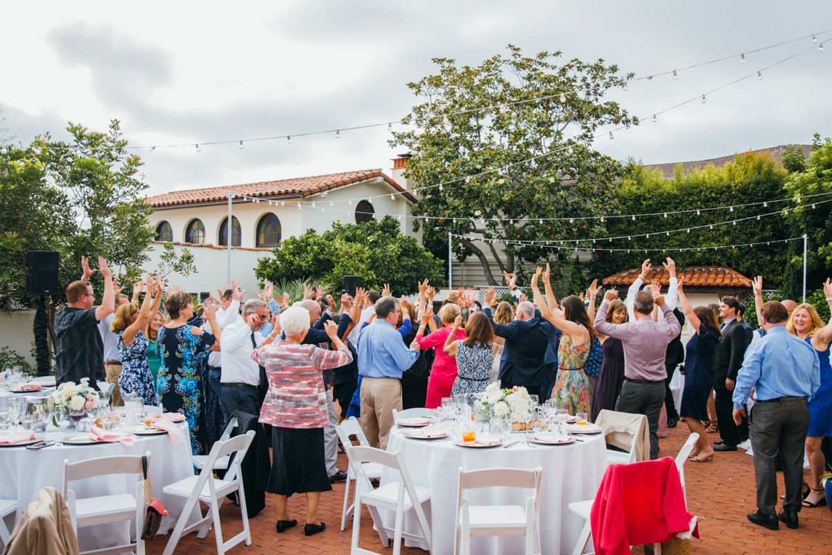 Wedding guests celebrate with raised hands at an outdoor reception under string lights.