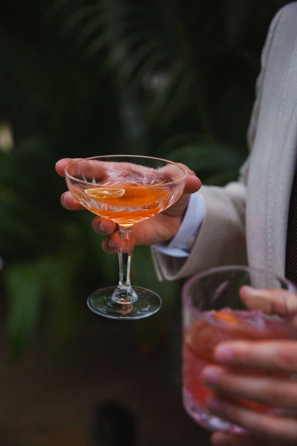 Groom holding an orange cocktail garnished with citrus peel at an outdoor wedding reception.