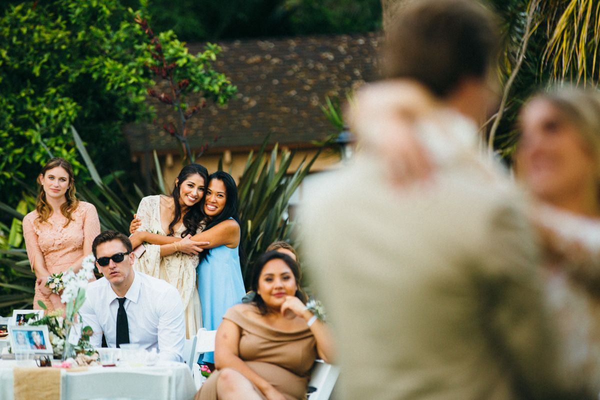 Guests smile and watch a couple share their first dance at an outdoor wedding reception.