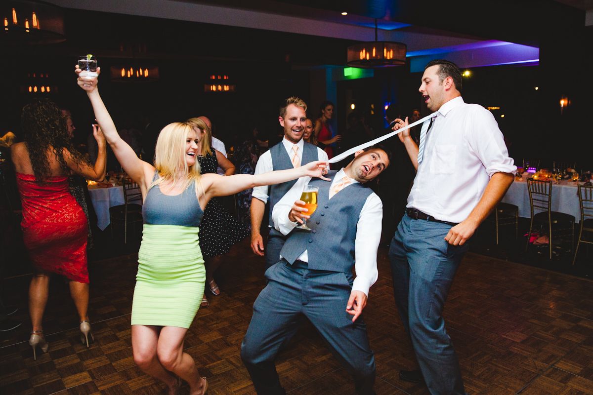 Wedding guests dance energetically on reception dance floor with colorful lighting in background.