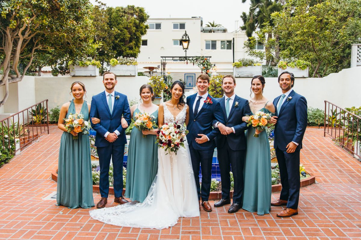 Wedding party poses together outdoors, bridesmaids in teal gowns and groomsmen in navy suits.