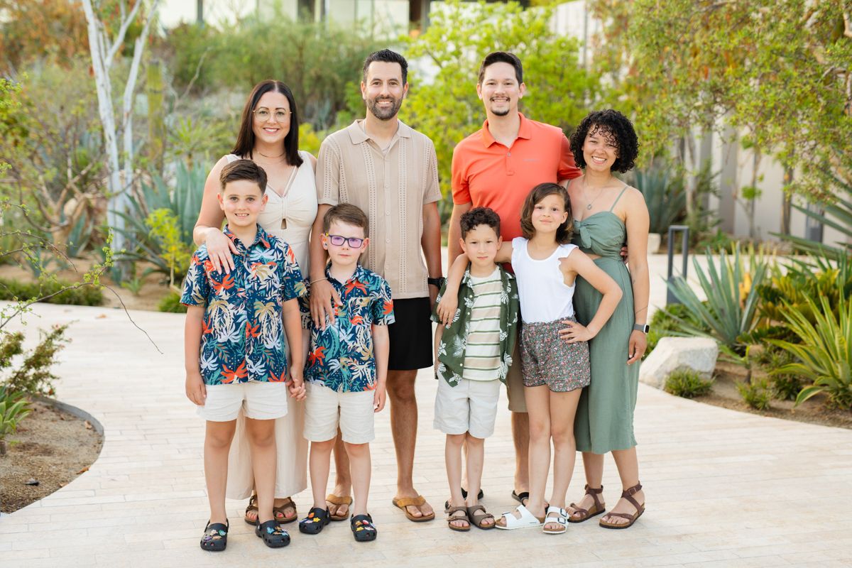 Extended family group portrait with four adults and five children outdoors in tropical setting.