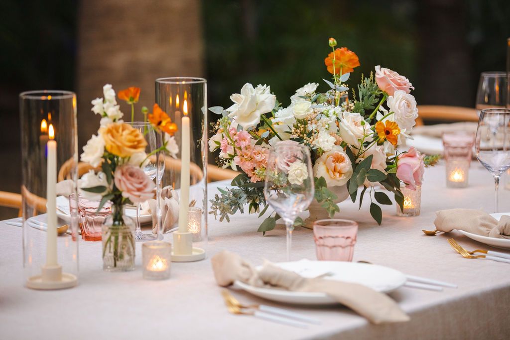 An elegant wedding reception table features lush floral centerpieces with peach and white blooms and candles.