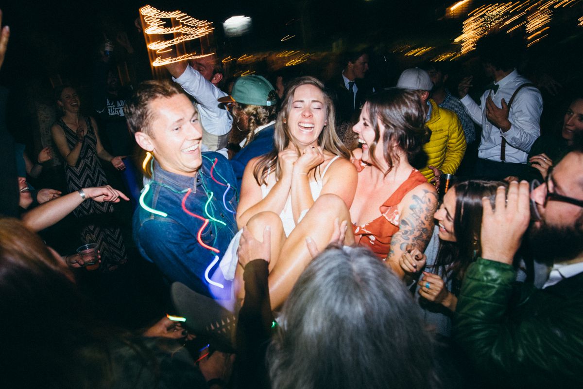 Joyful wedding guests dance and celebrate together on a crowded, dimly lit dance floor at a reception.