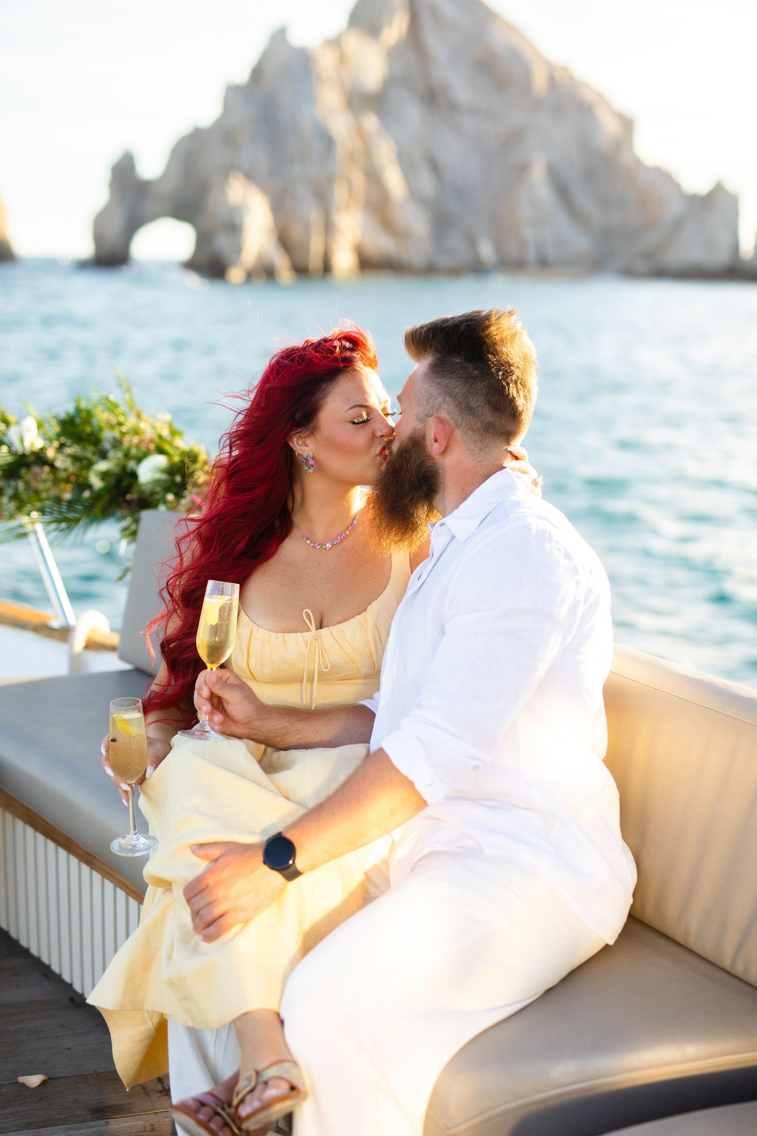 Couple kissing on a yacht with champagne near El Arco rock formation in Cabo San Lucas, Mexico.