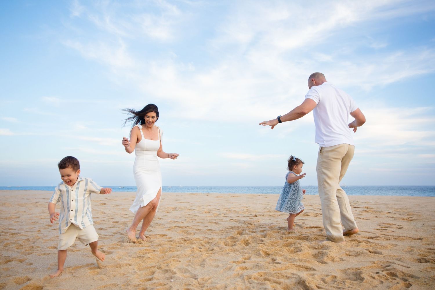 Family of four playing and dancing together on a sandy beach in Cabo San Lucas under a bright blue sky on a sunny day.