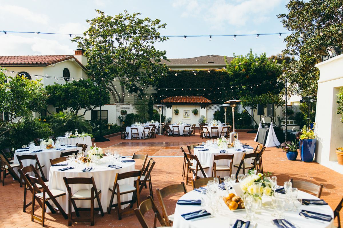 Elegant outdoor wedding reception with round tables, string lights, and Spanish-style architecture.